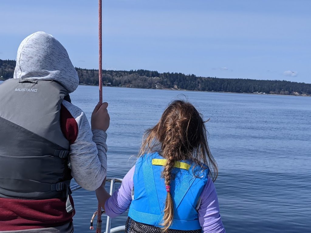 Kids watching orcas from the bow of our sailboat in the puget sound