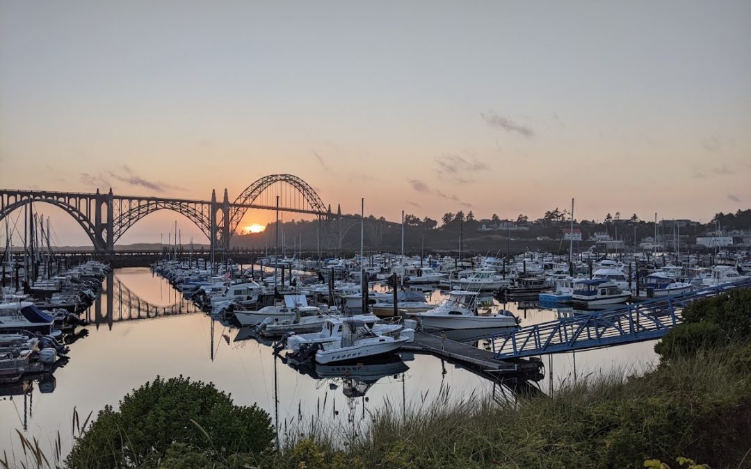 View of the sunset through the Newport Oregon bridge in a photo with the Port of Newport Marina in the foreground
